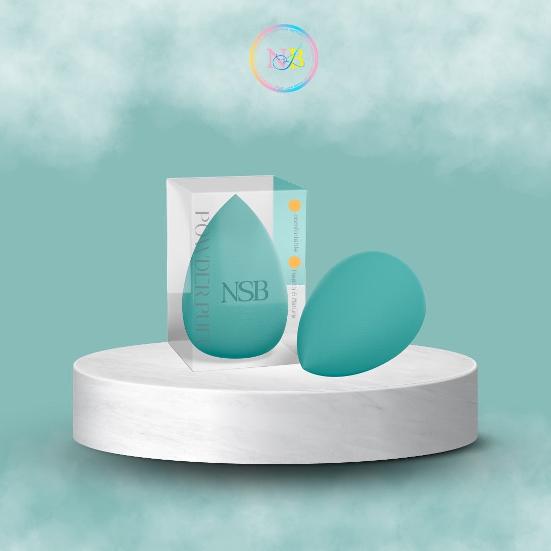 A latex-free NSB Beauty Blender in an aqua color is displayed on a round white platform. One soft sponge is enclosed in semi-transparent packaging marked with "NSB" and "POWDERPUFF" from the Nayy Seduction Brand, while another sponge sits beside the box. The background features a teal gradient with a subtle watermark logo on top.