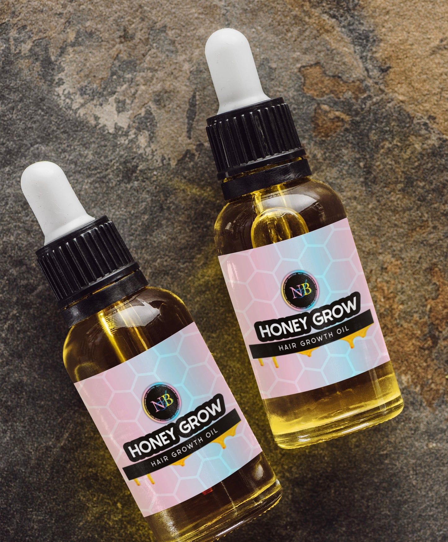 Two dropper bottles labeled "Honey Grow Hair Growth Oil (Rose Infused)" are displayed on a textured stone surface. Each bottle contains yellow oil and has a black cap with a white dropper. The pink labels feature a honeycomb pattern and the Nayy Seduction Brand logo, highlighting its blend of natural oils for dry scalp care and hair growth.